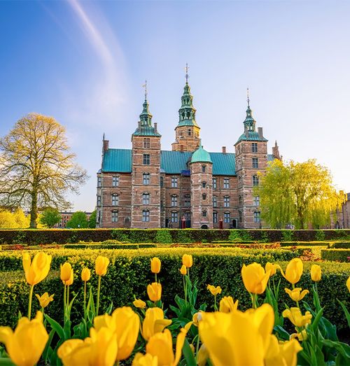 A stone palace capped with green rooftops with yellow tulips in the foreground