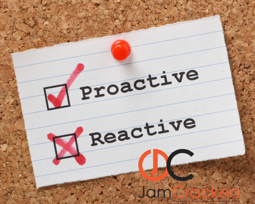 A cork noticeboard displaying a pinned lined note with two options: “Proactive” and “Reactive.” The “Proactive” option is ticked with a red check mark, while “Reactive” is crossed out. The JamCrackers logo and slogan “Making IT happen” appear in the bottom right corner.