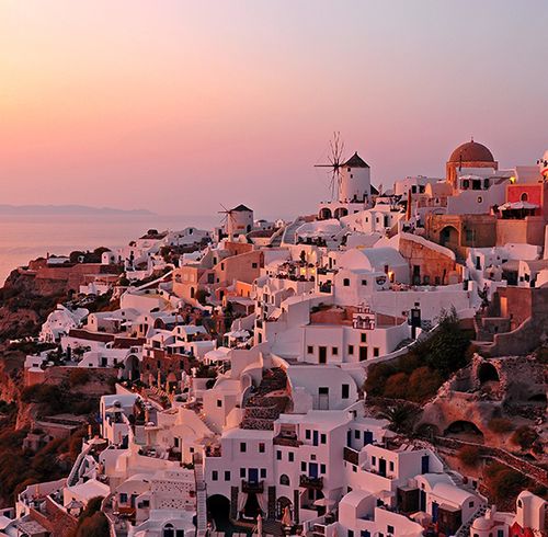 A gorgeous view of a city on a hillside made up of all white houses and buildings during a pink and orange sunset