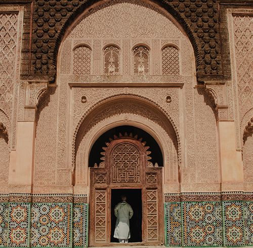 An extremely grand and ornate door with several distinct layers of detail including wood carvings and tile work with a man standing in the middle of the entrance