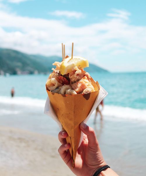 hand holding a cone filled with seafood by the water in cinque terre