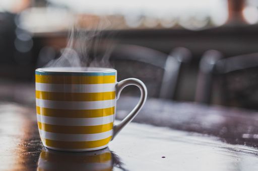 In home care- Photo of a yellow and white striped mug steaming sitting on a table in the foreground