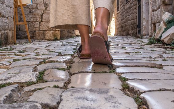 close up of woman walkin gin sandals down cobble stone street in italy