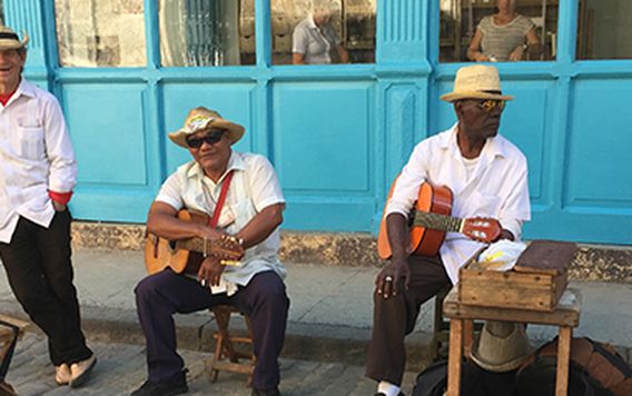 four cuban musicians sitting outside a bright blue building in havana