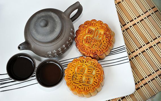chinese kettle with two cups and two mooncakes on a white dish