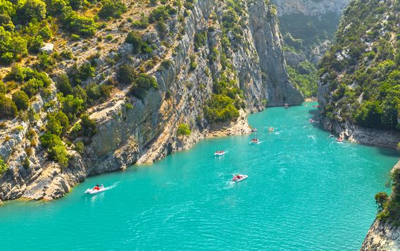people in floats boating down teal blue river in the verdon gorge in france