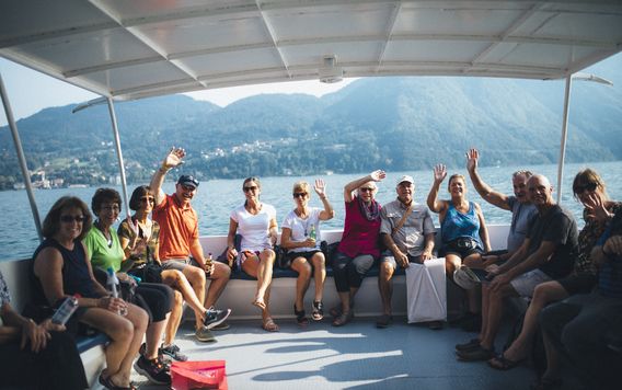 group of travelers waving at the camera from a boat on lake como in italy
