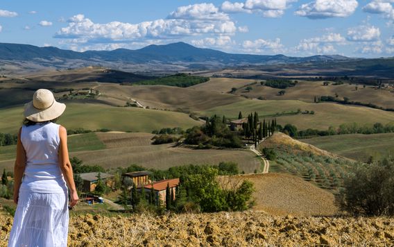 woman with a hat standing in the grass looking at the rolling hills in tuscany italy
