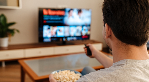 Muž s popcornem před televizí s ovladačem v ruce