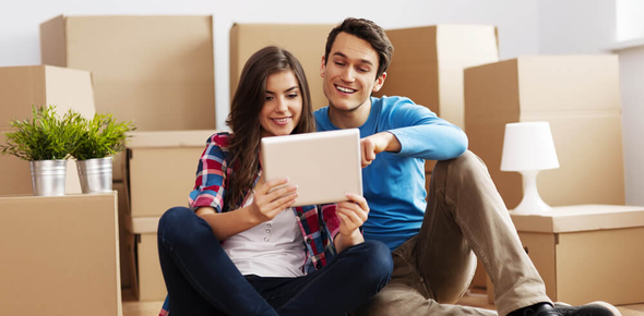 Půjčka na bydlení - mladý pár sedí na zemi mezi krabicemi a kouká do tabletu