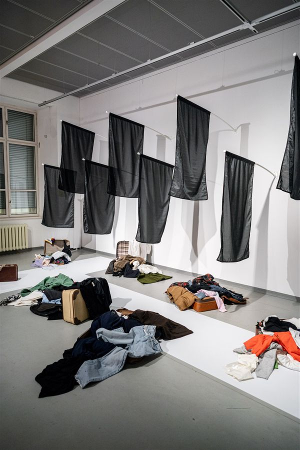 black flags hanging on wall, on the floor open suitcases with piles of clothes | Image by ©