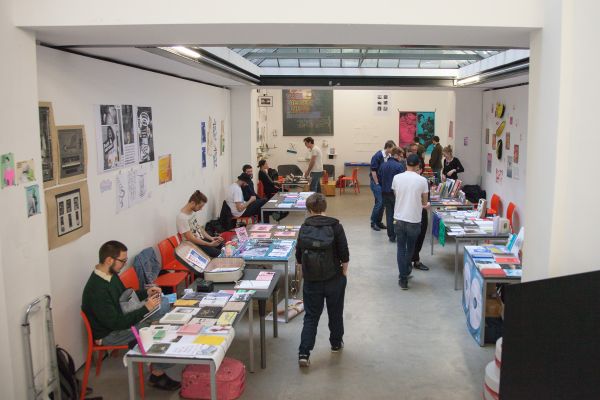 room with tables, prints, sellers and audience | Image by ©