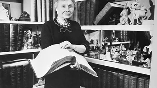 Black and White picture of Helen with a book in her hand. Behind her is a shelf of books