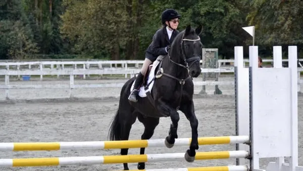 Blind rider jumping over the obstacle with her black horse 