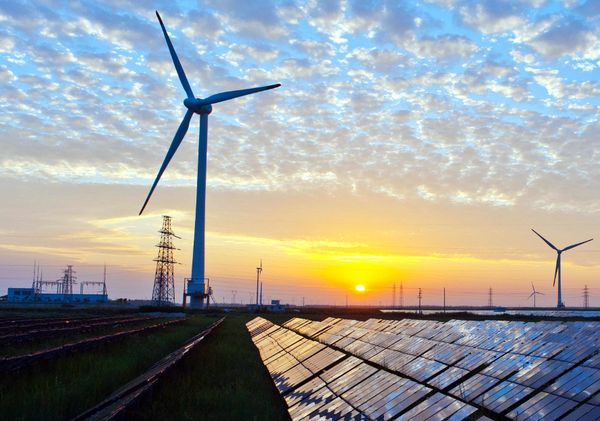 Wind turbines and solar panels in a field at sunset, with a cloudy sky and power lines in the background.