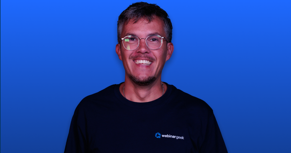 Smiling man with glasses wearing a black "webinargeek" T-shirt, set against a blue background.