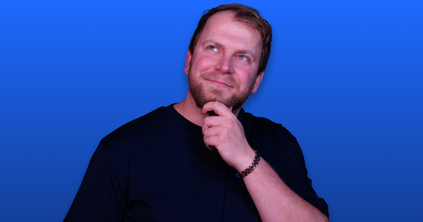 Man in a black shirt with a thoughtful expression, hand on chin, against a solid blue background.