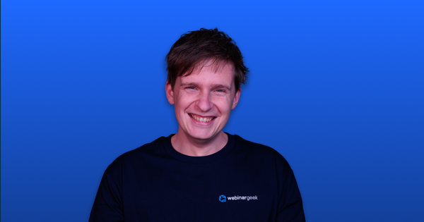 Smiling person wearing a black "webinargeek" shirt, against a blue gradient background.
