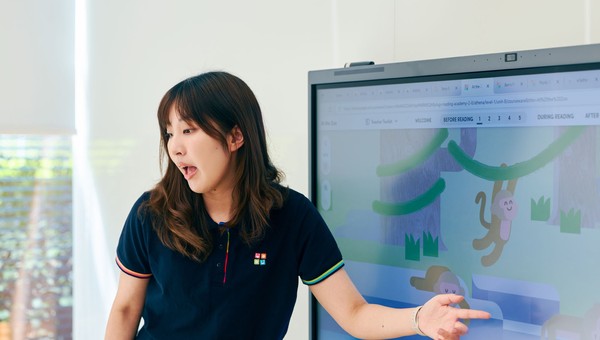 A woman in a navy shirt points at a digital screen displaying a playful monkey illustration, while explaining something.
