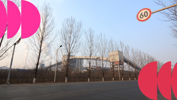 Industrial building behind leafless trees with a 60 km/h speed sign and pink graphic elements on the sides.