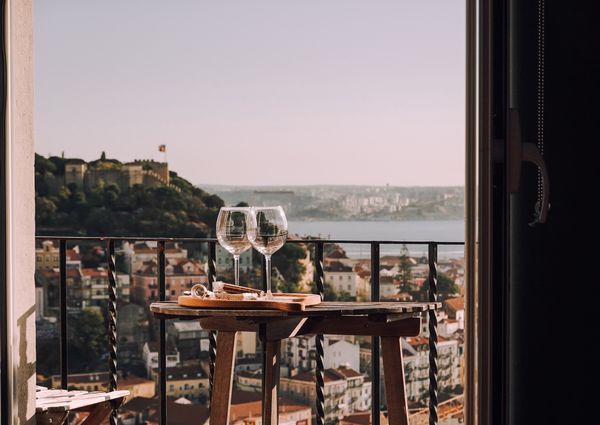 Two wine glasses set on a table on a balcony overlooking a city and water