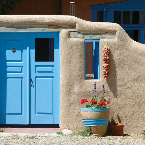 entrance to a tan clay house with a bright blue door and pot of red flowers