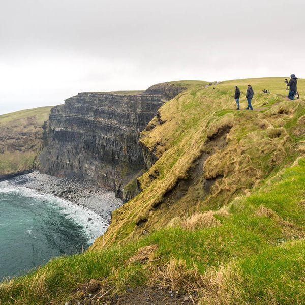 people walking along the cliffs of moher in ireland on cloudy day