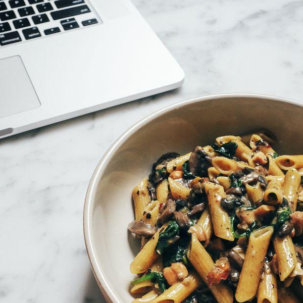 A plate of pasta on a table next to a laptop