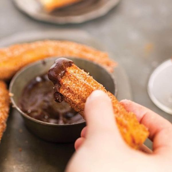 a hand dipping a churro in chocolate