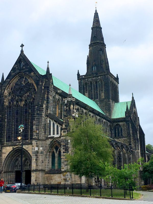 Glasgow cathedral, made of dark brown stone with an oxidize-copper colored roof in Scotland with a cloudy sky in the background