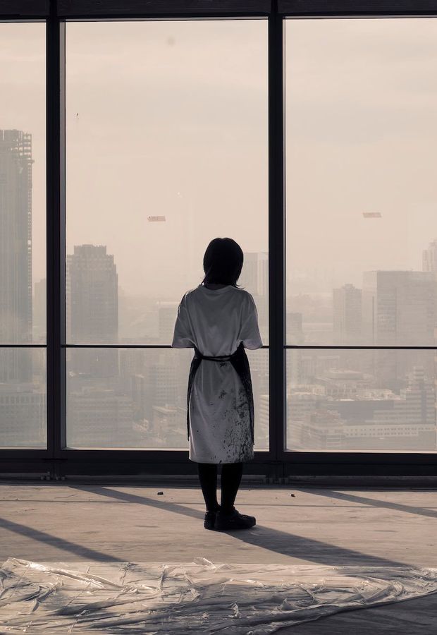 half-silhouetted artist looking out to a hazy cityscape through a row of floor to ceiling windows