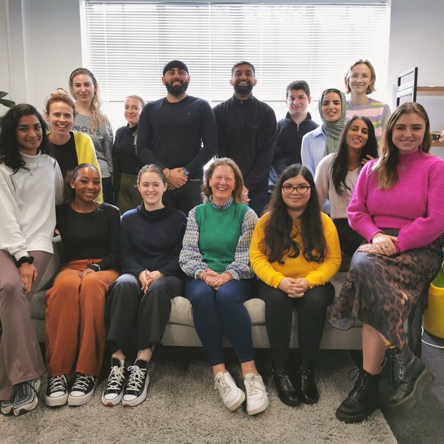 A full cohort of Flex Trainees are seen across a sofa in the Flex Legal office. They are as diverse as they are happy, and each bear a warming smile.