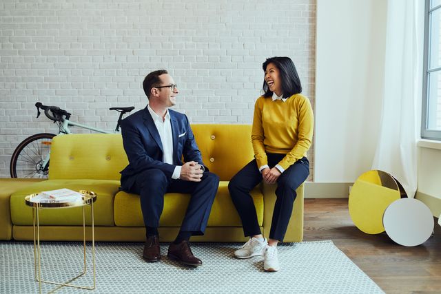 Teambild Businessfotografie Berlin Mann und Frau sitzen auf gelben Sofa und lachen Corporate Fotografie