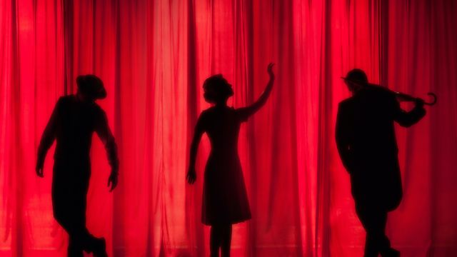 An image of three performers in silhouette against a red curtain.