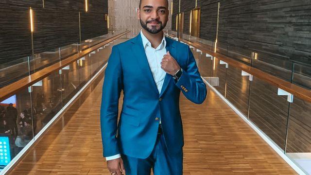 A picture of Mariano in a blue suit standing in a wooden-clad walkway.
