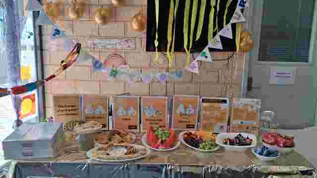 A decorated table with snacks, fruits, and instructional posters for R U OK? Day. Gold balloons and colorful garlands hang above.