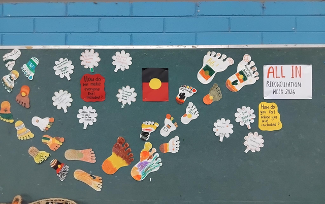 Bulletin board with colorful footprints, speech bubbles about inclusion, Aboriginal flag, and "All In Reconciliation Week 2026" sign.