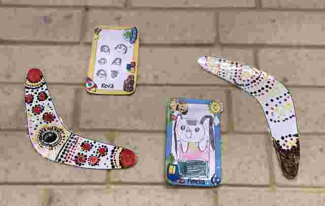 Handmade boomerangs and portraits with colorful patterns and drawings, displayed on a tiled surface.