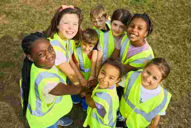 Children smiling with their hands together in a circle outside