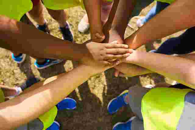 Children with their hands together in a circle outside