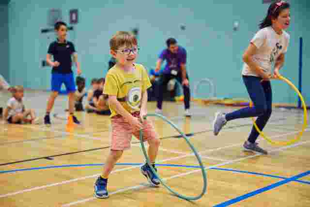 Children playing with a hula hoop in a sports hall