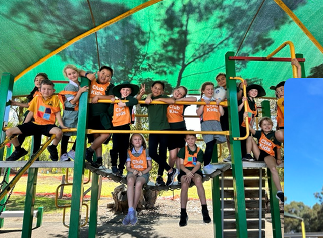 Children in colorful shirts and hats smile while sitting on playground equipment under a green canopy, with trees in the background.