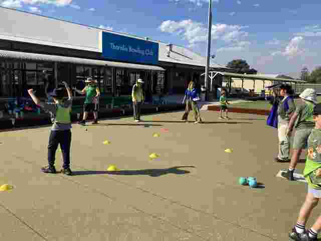 Children playing a game with colored cones on a lawn at Thornlie Bowling Club, led by adults in bright vests.