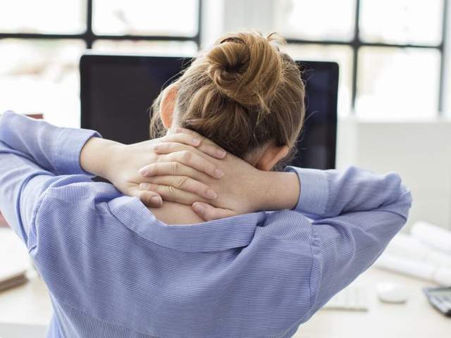 Frau sitzt vor dem Computer und umschließt Nacken mit beiden Händen