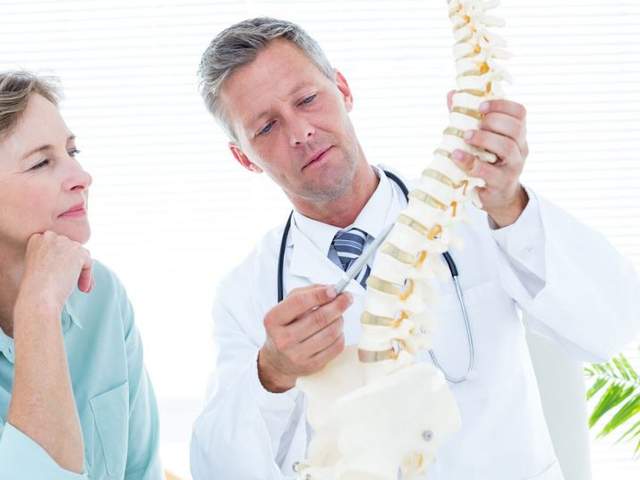 Arzt erklärt Patientin den Bandscheibenvorfall am künstlichen Skelett