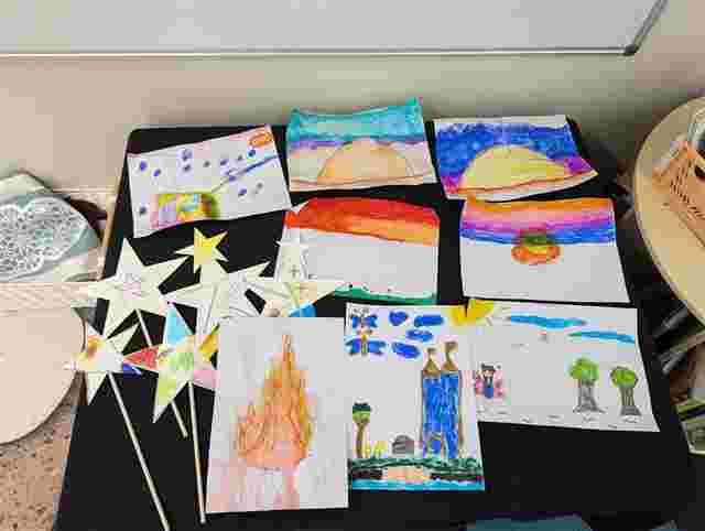 Colorful children's artwork displayed, featuring landscapes, stars on sticks, and various creative drawings on a black surface.