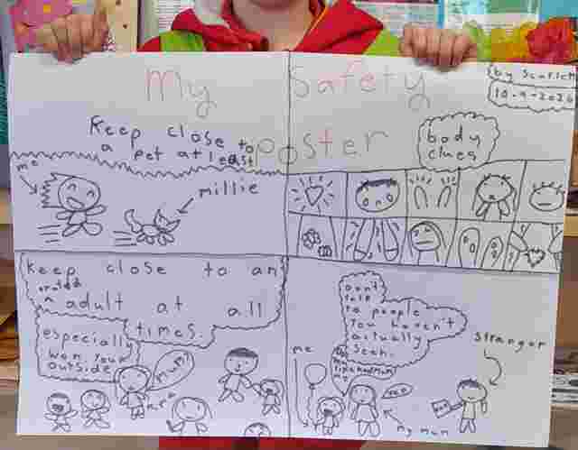A child holds a safety poster with drawings of stick figures and text: "Keep close to a pet," "Body clues," "Stay close to a trusted adult," "Don't talk to strangers."