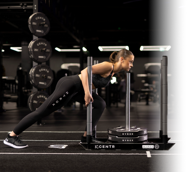 A girl pushing a Centr HYROX Race day sled, with HYROX weights in Puma HYROX leggings