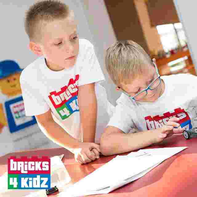 Two children in "Bricks 4 Kidz" shirts engage in a building activity at a table with LEGO pieces and instructions.