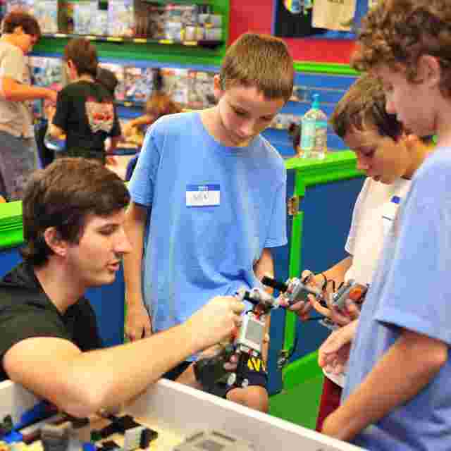 A group of children and an adult engage in building with LEGO bricks at a colorful indoor play area.